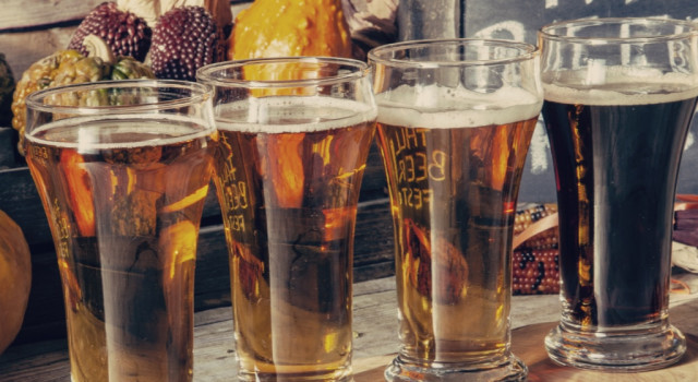 Pints of beer in front of seasonal fall vegetables.